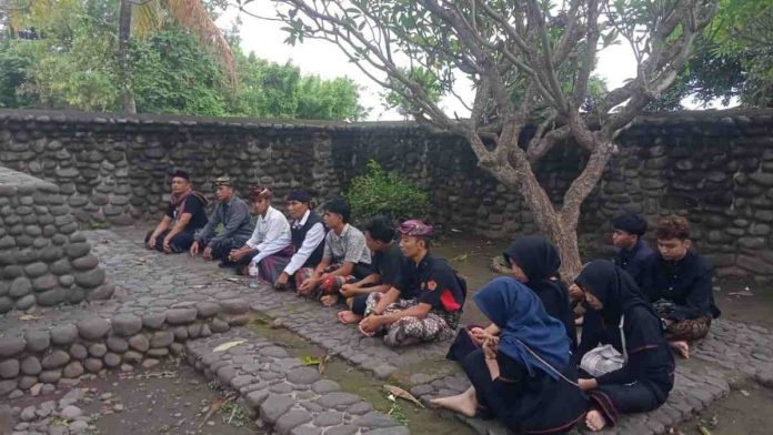 Kelompok masyarakat Suku Sasak sedang duduk bersimpuh mendoakan leluhur dalam tradisi mersin puasa di area pemakaman batu tradisional Lombok.