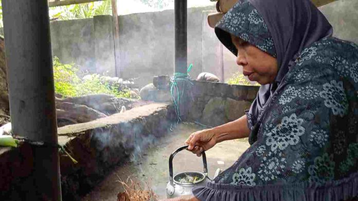Seorang wanita berhijab sedang memegang teko berisi air dan kembang di tengah kepulan asap kemenyan dalam sebuah ritual adat Suku Sasak.
