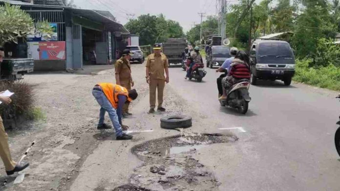 Petugas berbaju oranye dan ASN Dinas PUPR NTB memeriksa lubang besar di tengah jalan raya jalur Praya-Keruak yang tergenang air.