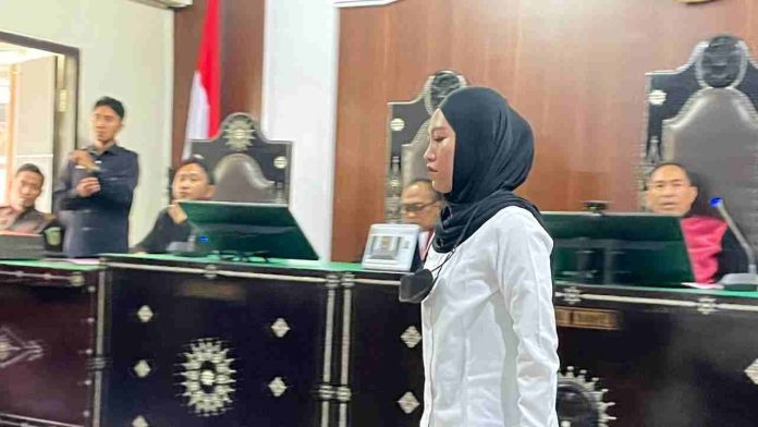 Terdakwa Brigadir Rizka Sintiyani mengenakan kemeja putih dan kerudung hitam berdiri di ruang sidang Pengadilan Negeri Mataram.