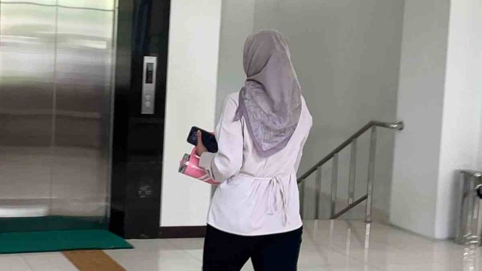 Logopit_1770877244114 Seorang wanita berjilbab abu-abu dan baju putih tampak belakang sedang berjalan di koridor gedung Kejati NTB sambil membawa botol minum berwarna pink dan ponsel.