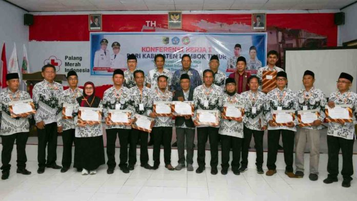 Bupati Lombok Timur Haerul Warisin bersama belasan pengurus PGRI mengenakan seragam batik resmi organisasi (batik Kusuma Bangsa) berpose memegang piagam penghargaan di depan spanduk Konferensi Kerja I PGRI di Aula PMI Lombok Timur.