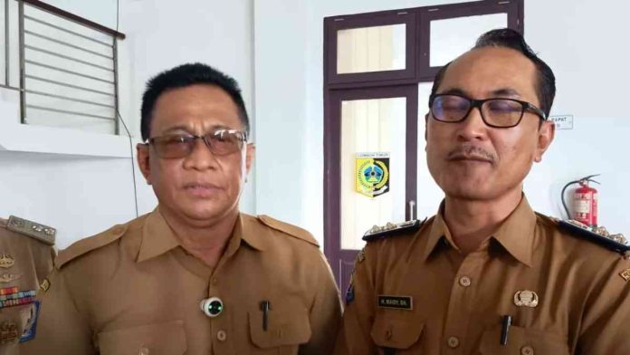Dua pria berseragam dinas cokelat (PNS/Aparatur Desa) berdiri berdampingan di dalam ruangan.