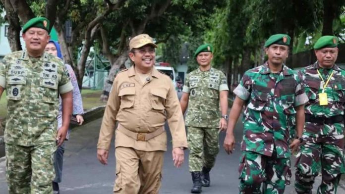 Bupati Lombok Barat Lalu Ahmad Zaini mengenakan seragam cokelat dan topi, berjalan bersama perwira TNI berpakaian dinas loreng di area Makorem 162/Wira Bhakti dalam acara pembukaan Capacity Building.