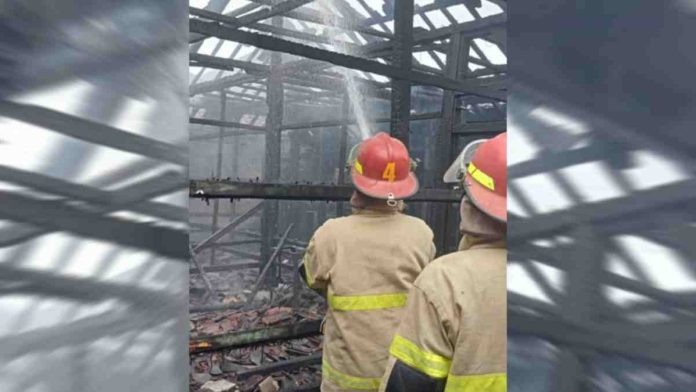 Dua petugas Damkar helm merah menyemprotkan air ke rangka atap kayu yang hangus terbakar di area pemukiman padat penduduk Kabupaten Lombok Timur.