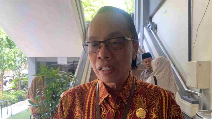 Potret Asisten 1 Setda Kota Mataram Lalu Martawang mengenakan batik cokelat dan kacamata saat memberikan pernyataan resmi di depan awak media.