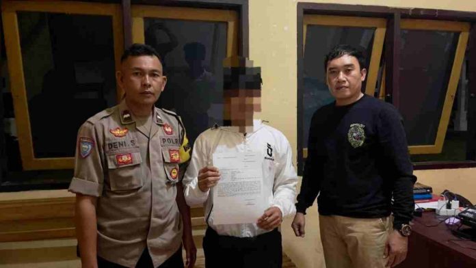 Logopit_1771252303894 Dua polisi mengapit terduga pelaku berjaket putih yang memegang surat keterangan di kantor polisi dengan wajah disensor demi privasi hukum.