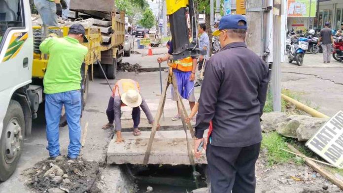Petugas konstruksi Dinas PUPR NTB mengangkat pelat beton menggunakan crane di pinggir jalan provinsi Lombok Timur untuk memperbaiki saluran drainase yang tersumbat sampah.