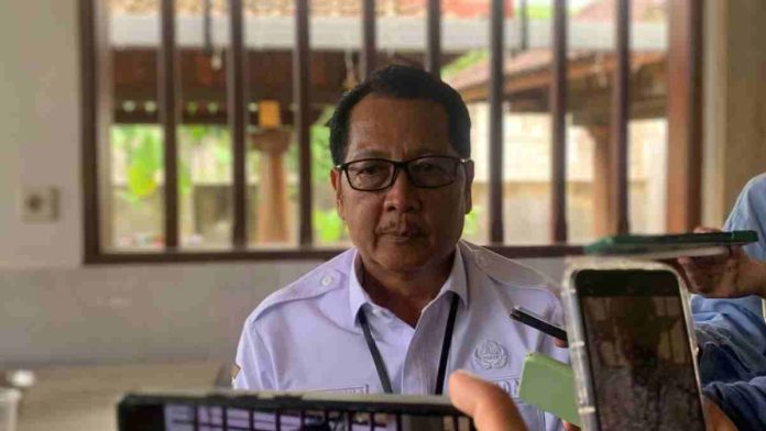 Foto Sekda Kota Mataram Lalu Alwan Basri mengenakan seragam dinas putih dan kacamata saat diwawancarai oleh wartawan yang memegang ponsel dan alat perekam di depannya.