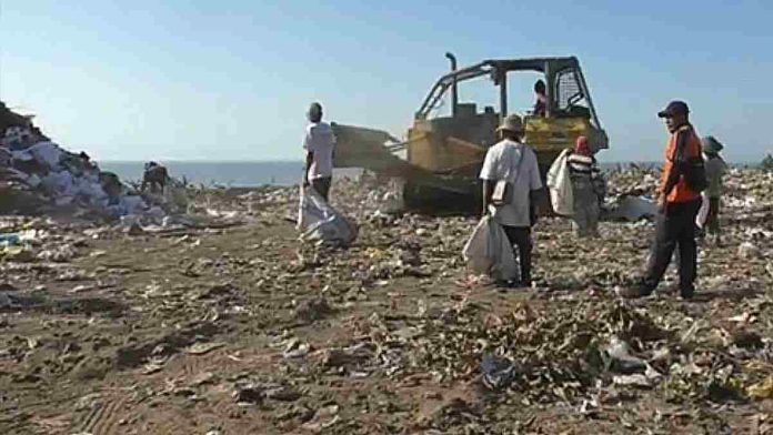 Logopit_1771660141699. Kondisi tumpukan sampah di TPA Ijo Balit Lombok Timur dengan latar belakang aktivitas alat berat dan petugas kebersihan.