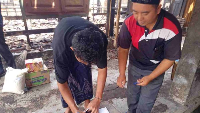 Petugas Baznas Lombok Timur sedang mendata dan menyerahkan bantuan berupa beras serta sembako kepada korban kebakaran di depan reruntuhan rumah.