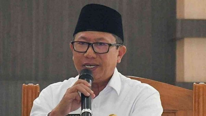 Foto profil Kepala BKAD Lombok Timur Hasni mengenakan baju putih, kacamata, dan peci hitam saat sedang berbicara menggunakan mikrofon dalam sebuah pertemuan resmi