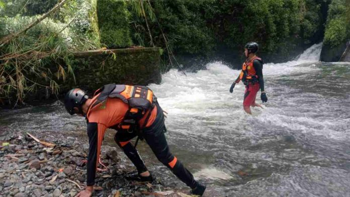 Dua petugas SAR mengenakan seragam oranye, pelampung, dan helm pelindung sedang menyisir aliran sungai yang berarus deras di area pegunungan Sembalun untuk mencari korban hilang.
