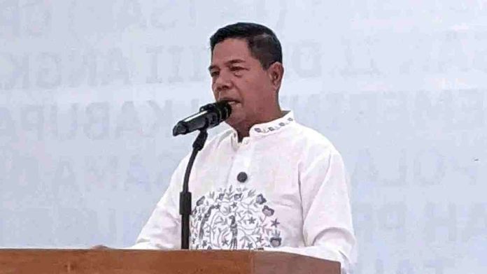 Bupati Lombok Timur H. Haerul Warisin mengenakan kemeja putih motif bordir di dada, sedang berbicara di depan mikrofon dalam sebuah acara resmi.