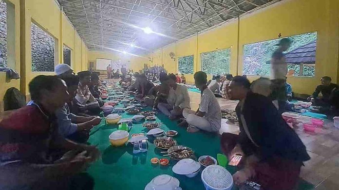 Sekelompok pria duduk bersila di atas karpet hijau dalam sebuah ruangan besar sambil menikmati hidangan buka puasa bersama yang disusun memanjang dalam acara silaturahmi Palasmasta NTB.