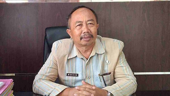 Kepala Bapenda Lombok Timur, Muksin, mengenakan seragam dinas cokelat motif garis, duduk di ruang kerjanya sambil memberikan keterangan terkait capaian Pendapatan Asli Daerah (PAD).