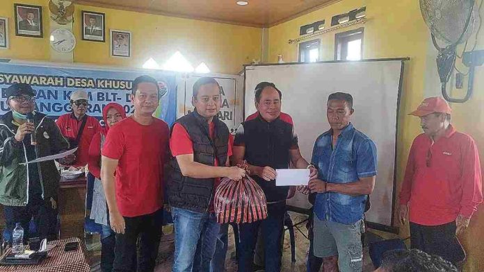 Abdul Rafiq mengenakan rompi hitam menyerahkan paket bantuan dan amplop tunai kepada warga terdampak kebakaran dalam acara musyawarah desa di Desa Kalimango, Sumbawa.