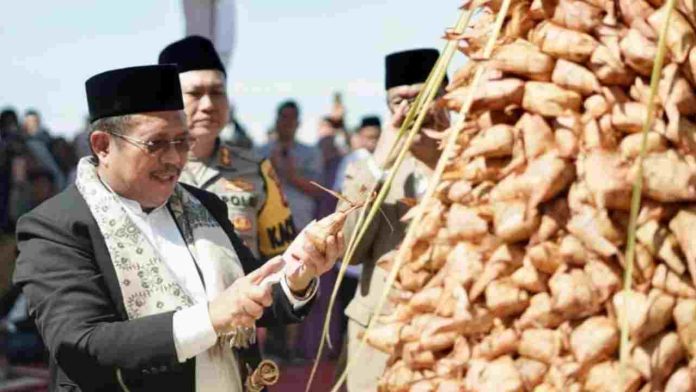 Bupati Lombok Barat mengenakan jas dan peci hitam sedang memotong gunungan ketupat raksasa pada perayaan Lebaran Topat di Senggigi, didampingi pejabat Polri dan TNI.
