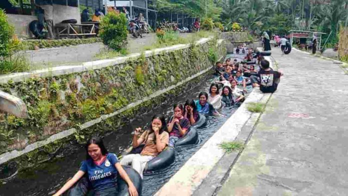 Pengunjung memadati kolam pemandian Wisata Reban Batu Lombok Timur dengan latar pemandangan sawah hijau yang asri.