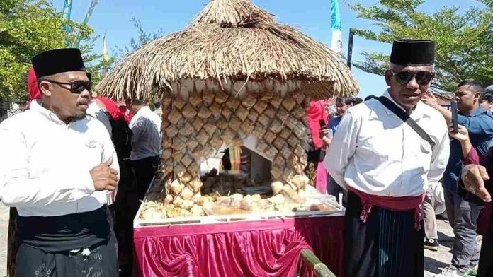 Dua orang pria berpakaian adat Sasak berdiri di samping gunungan ketupat raksasa dalam perayaan Tradisi Lebaran Topat di Kota Mataram.