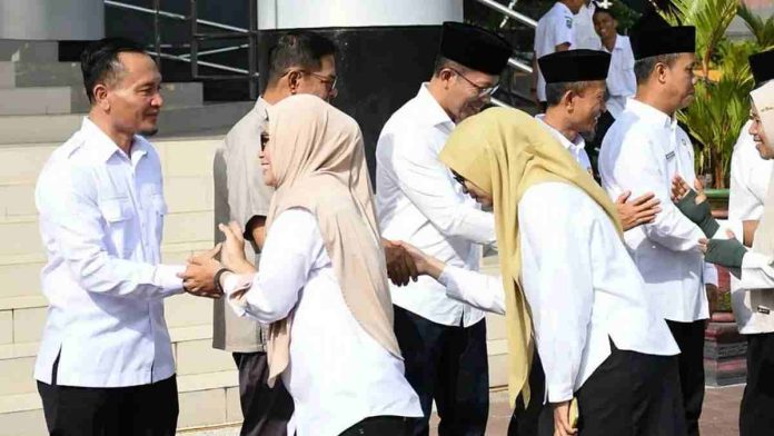 Bupati Lombok Timur H. Haerul Warisin mengenakan kemeja putih bersalaman dengan barisan pegawai ASN laki-laki dan perempuan di depan tangga Kantor Bupati.