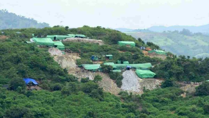 Pemandangan lereng bukit hijau yang dipenuhi dengan tenda-tenda terpal berwarna hijau dan biru sebagai lokasi aktivitas penambangan rakyat di Nusa Tenggara Barat.