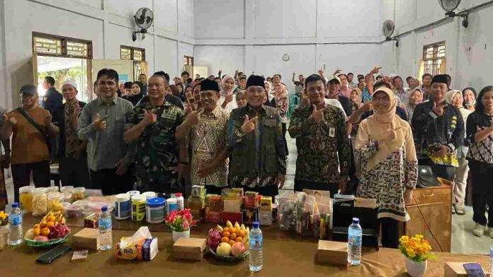 Sekelompok orang berfoto bersama di dalam ruangan, berpose menunjuk dengan satu jari. Di depan mereka terdapat meja penuh sampel produk obat, kosmetik, dan makanan hasil pengawasan.