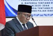 Kemiskinan Lombok Utara Turun Drastis di Bawah Kepemimpinan Najmul Akhyar Bupati Lombok Utara Najmul Akhyar mengenakan jas abu-abu dan peci hitam, sedang membacakan dokumen LKPJ di podium dalam rapat paripurna DPRD.