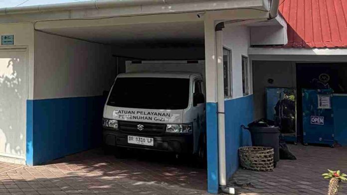 Sebuah mobil pikap putih dengan tulisan Satuan Pelayanan Pemenuhan Gizi terparkir di garasi gedung berwarna putih biru yang merupakan kantor Badan Gizi Nasional tingkat satuan pelayanan.