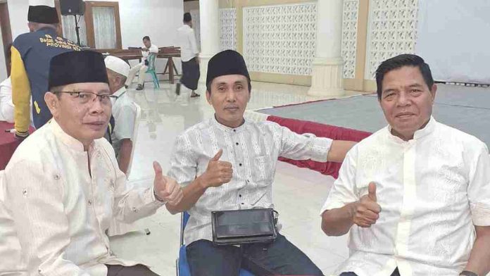Tiga orang pria mengenakan baju koko putih dan peci hitam duduk berjajar sambil memberikan pose jempol di dalam sebuah ruangan pertemuan dengan latar belakang tiang putih.