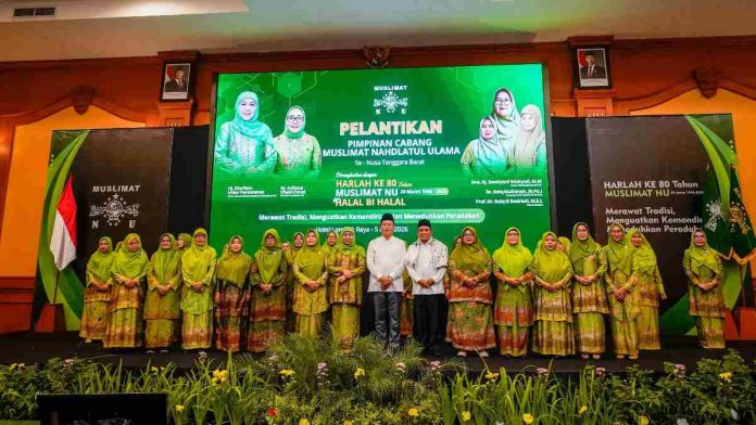 Gubernur NTB Lalu Muhammad Iqbal berdiri di tengah barisan pengurus Muslimat NU yang mengenakan seragam hijau batik khas organisasi di atas panggung dengan latar layar LED besar.