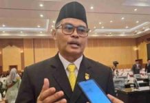 Abdul Malik Dukung Penyelamatan Lahan Sawah Mataram Tekankan Sinkronisasi Data Foto close-up Ketua DPRD Kota Mataram, H. Abdul Malik, mengenakan jas hitam, peci, dan dasi kuning, sedang memberikan pernyataan di depan mikrofon wartawan dalam sebuah ruangan.