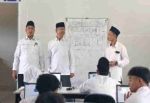 10.870 Siswa MTs Lombok Timur Ikuti TKA Kemenag Pastikan Ujian Lancar Tiga orang pria mengenakan kemeja putih dan peci hitam berdiri di depan kelas memantau siswa yang sedang mengerjakan ujian di depan komputer masing-masing. Di belakang mereka terdapat papan tulis putih.