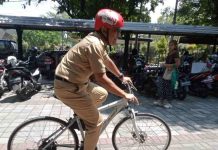 Gowes ke Kantor Belum Aman, Dishub Mataram Kelimpungan Cari Jalur Seorang pria berseragam ASN cokelat mengenakan helm merah sedang mengendarai sepeda perak di area parkir yang dipenuhi deretan sepeda motor.