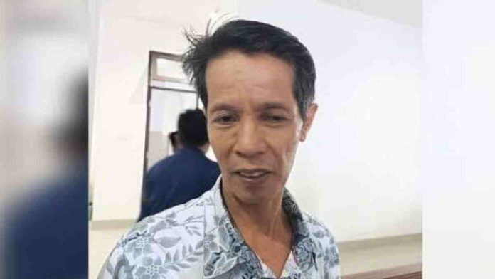 Potret close-up wajah Kepala Dinas PMD Lombok Timur, Hambali, yang mengenakan kemeja motif batik biru muda saat memberikan keterangan di dalam ruangan.