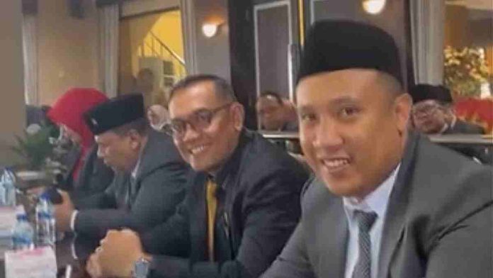 Ahmad Azhari Gufron (tengah) bersama rekan anggota dewan lainnya mengenakan jas formal dan peci hitam duduk dalam sebuah acara resmi di gedung DPRD.