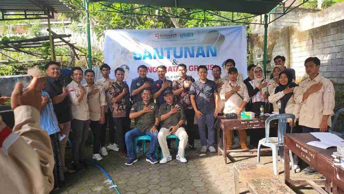 Sekelompok pria dan wanita berfoto bersama di depan spanduk acara bertuliskan Santunan & Pengobatan Gratis, berpose dengan tangan di dada sebagai simbol solidaritas di Sakra.