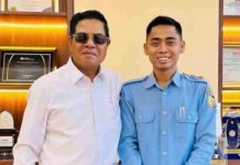 PDAM Lombok Timur Siap All Out Dukung Makan Gratis dan Koperasi Desa Dua pria berdiri berdampingan di dalam ruangan dengan latar belakang lemari pajangan berisi piagam dan piala. Pria di sebelah kiri mengenakan kemeja putih dan kacamata hitam. Pria di sebelah kanan mengenakan seragam dinas PDAM berwarna biru muda dan tersenyum ke arah kamera.