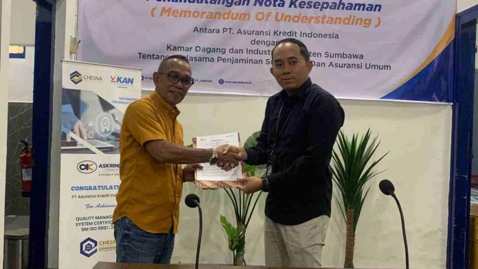 Dua pria berpakaian kasual rapi sedang bersalaman sambil memegang map dokumen kerja sama di depan latar spanduk penandatanganan Nota Kesepahaman antara PT Asuransi Kredit Indonesia dan Kadin Sumbawa.