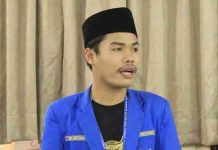 PMII Lotim Desak Pemda Segera Bangun Rumah Sakit di Pringgabaya Yogi Setiawan, Ketua PC PMII Lombok Timur mengenakan jas biru dan peci hitam, sedang memberikan pernyataan terkait tuntutan pembangunan rumah sakit di Kecamatan Pringgabaya.