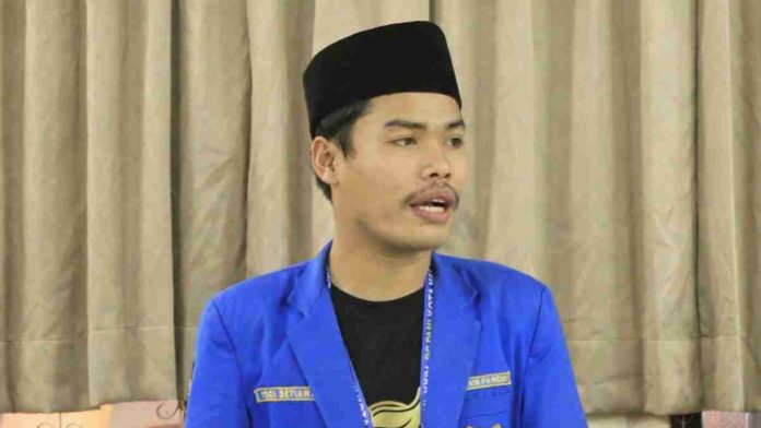 Yogi Setiawan, Ketua PC PMII Lombok Timur mengenakan jas biru dan peci hitam, sedang memberikan pernyataan terkait tuntutan pembangunan rumah sakit di Kecamatan Pringgabaya.