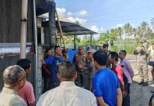 Satgas temukan Kandang Ayam Pakai Gas Melon, Sekda Lombok Timur Beri Waktu Tiga Hari Sejumlah petugas Satpol PP dan pejabat daerah sedang berdialog dengan pengelola peternakan di depan sebuah bangunan kandang ayam. Para petugas mengenakan seragam dinas, sementara pengelola menggunakan kaus biru. Suasana luar ruangan di bawah cuaca cerah dengan latar pohon kelapa.