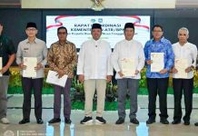 Menteri ATR BPN Nusron Wahid Serahkan Sertipikat Aset Strategis Kota Mataram Sembilan pria berdiri berjejer di dalam aula rapat dengan latar belakang layar digital bertuliskan "Rapat Koordinasi Kementerian ATR/BPN". Sebagian besar mengenakan kemeja formal dan peci hitam, sambil memegang map berisi sertipikat tanah. Di tengah rombongan tampak Menteri ATR/BPN Nusron Wahid mengenakan baju koko putih dan peci hitam.