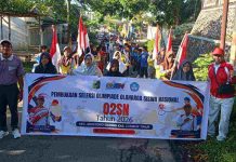 Karnaval Meriah Buka Seleksi O2SN Montong Gading Lombok Timur 2026 Sekelompok siswa dan guru berdiri di jalan aspal sambil memegang spanduk besar bertuliskan "Pembukaan Seleksi Olimpiade Olahraga Siswa Nasional O2SN Tahun 2026 Kec. Montong Gading Kab. Lombok Timur". Beberapa siswa di barisan belakang membawa bendera Merah Putih, sementara suasana di sekitar lokasi tampak asri dengan pepohonan hijau.