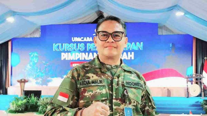 Close-up Abdul Malik mengenakan seragam loreng dengan papan nama bertuliskan namanya. Latar belakang panggung acara Kursus Pemantapan Pimpinan Daerah.