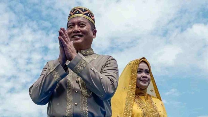 Lalu Muhamad Iqbal mengenakan busana adat cokelat emas dan sapu (ikat kepala) khas NTB berdiri di depan Hj. Indah Dhamayanti Putri yang mengenakan busana kuning cerah