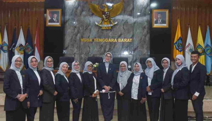 Sekelompok pengurus YKI NTB mengenakan seragam jas hitam dan hijab abu-abu berpose bersama di depan lambang Garuda Pancasila dan tulisan Nusa Tenggara Barat.