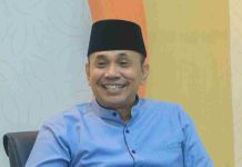 Lalu Iqbal Tempuh Jalur Hukum, Ini Penjelasan Resmi Pemprov NTB Potret Dr. H. Ahsanul Khalik mengenakan kemeja biru dan peci hitam, tampak tersenyum ramah saat memberikan keterangan di dalam ruangan.