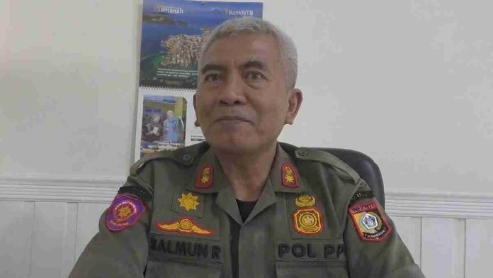 Potret Kasat Pol PP Lombok Timur Salmun Rahman mengenakan seragam dinas PDL cokelat lengkap dengan atribut pangkat, sedang duduk memberikan penjelasan.