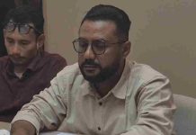 Eksekusi Tiga SPBU di Lombok Utara Dinilai Janggal Hingga Desak RDP DPR RI Foto seorang pria berkacamata dan berjenggot mengenakan kemeja krem, Fuad, S.H., sedang menunduk serius saat memberikan keterangan pers dalam sebuah ruangan.